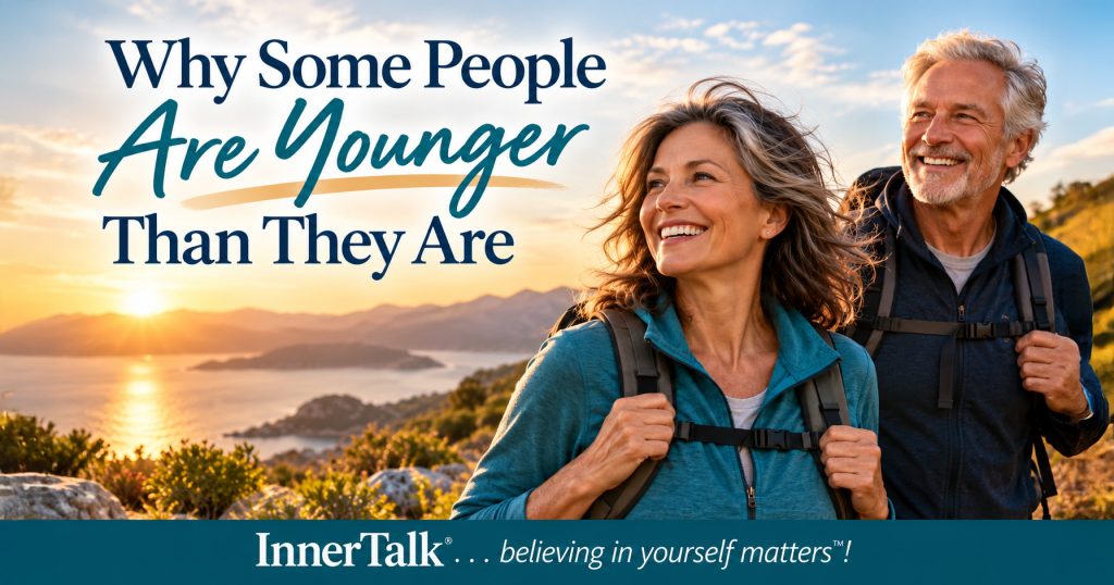 Active older couple hiking together beside the water at sunset. Text reads Why Some People Are Younger Than They Are.